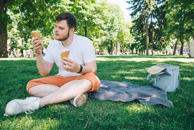 jovem adulto feliz comendo sorvete enquanto sentado no chão no parque da cidade em um dia quente de verão