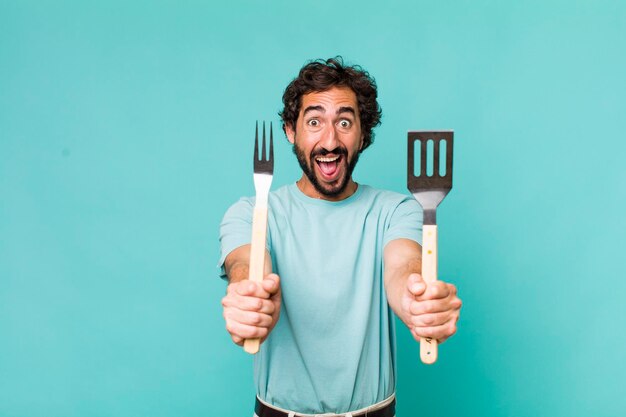 Jovem adulto hispânico louco com ferramentas de churrasco