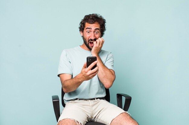 Jovem adulto hispânico louco usando seu telefone sentado em uma cadeira