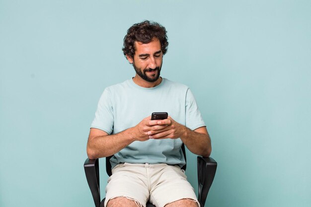 Jovem adulto hispânico louco usando seu telefone sentado em uma cadeira