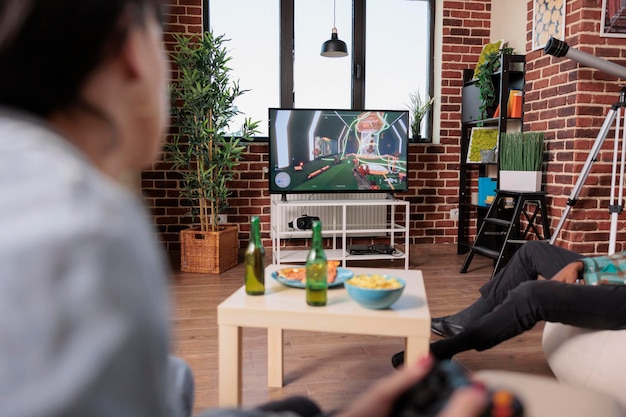 Foto jovem adulto jogando estratégia de videogame em casa, se divertindo com os amigos na festa em casa. competição de jogos no encontro com garrafas de cerveja e lanches, entretenimento.