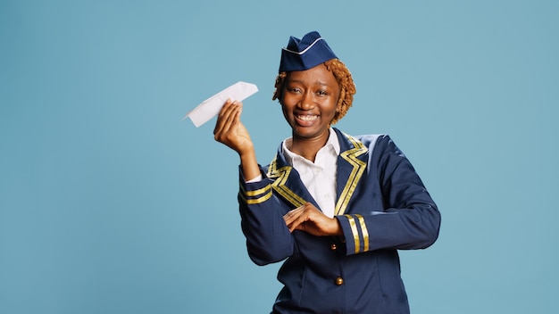 Jovem adulto mostrando avião de origami na câmera, brincando com avião de papel vestido de aeromoça. membro da tripulação profissional em uniforme segurando aeronaves dobradas no estúdio sobre o fundo.