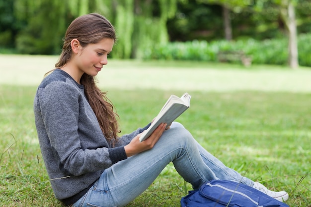 Jovem adulto relaxado lendo um livro sentado na grama