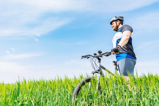 Jovem adulto sorridente em pé com bicicleta em cevada verde fi