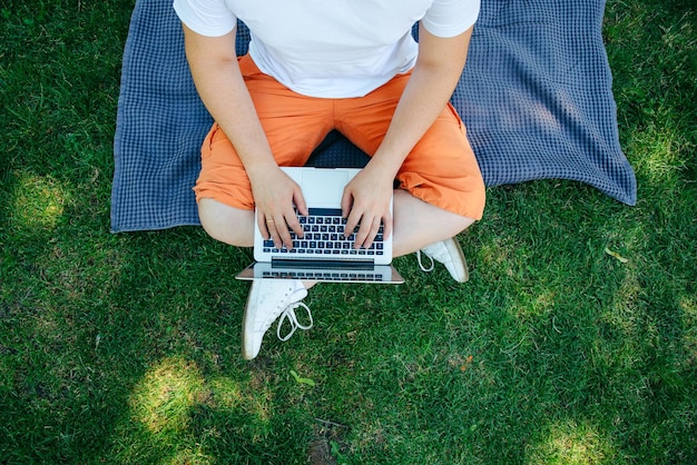 jovem adulto trabalhando em um laptop no parque da cidade em um dia de verão