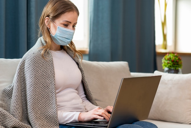 Foto jovem adulto usando uma máscara de proteção e trabalhando no laptop