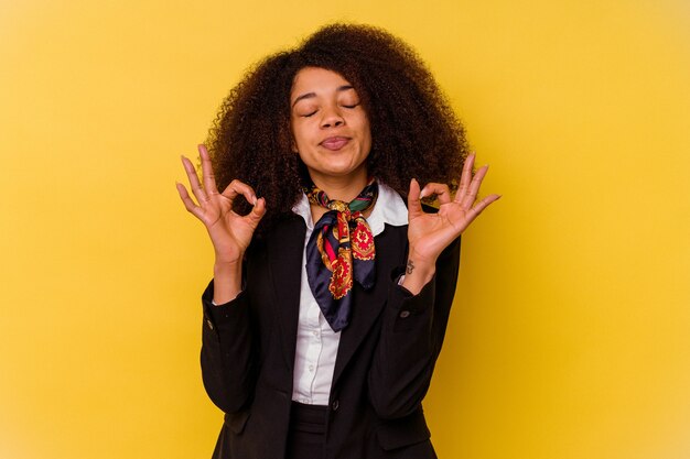 Jovem aeromoça afro-americana isolada em fundo amarelo relaxa após um árduo dia de trabalho, ela está realizando ioga.