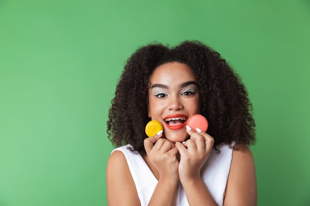 Jovem africana alegre com um vestido isolado, mostrando macaroons coloridos