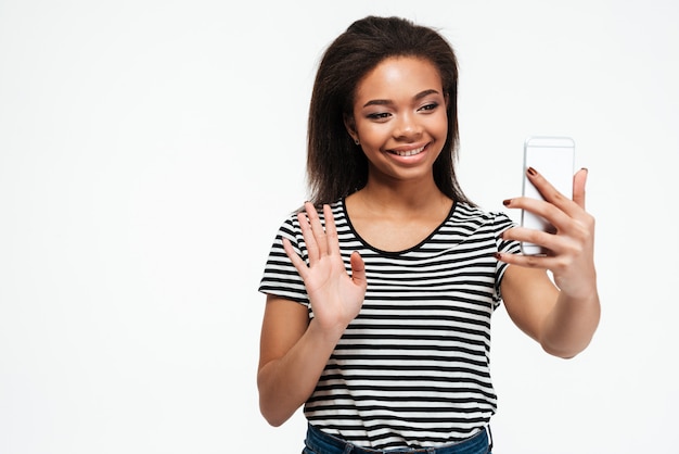 Jovem africana alegre falando por telefone e acenando.