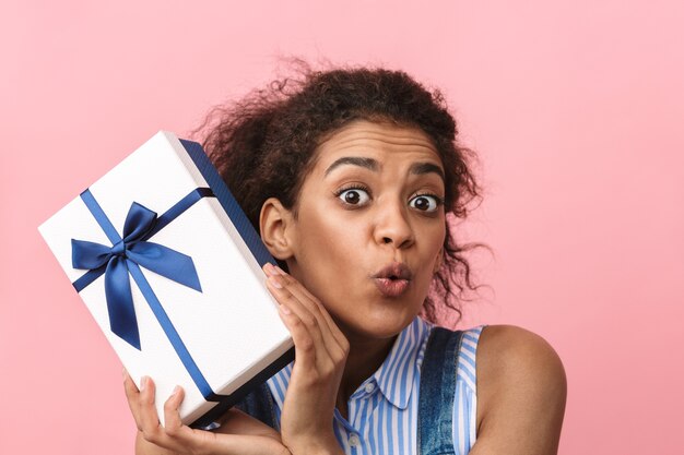 Jovem africana bonita e animada segurando uma caixa de presente rosa