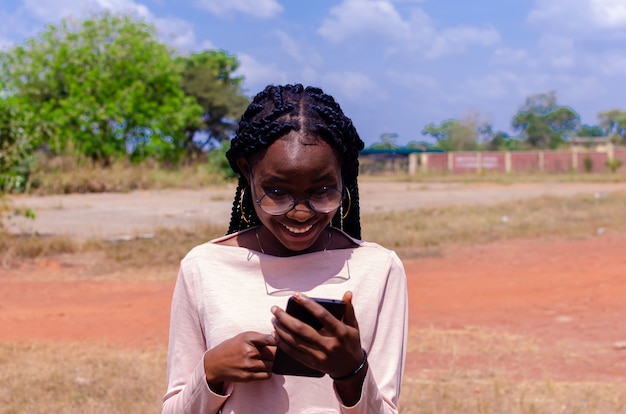 Jovem africana em um campo operando alegremente seu telefone