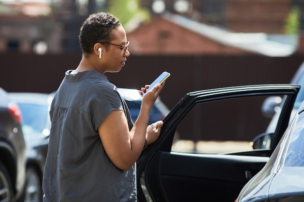 Jovem africana lendo uma mensagem no celular enquanto entra no carro