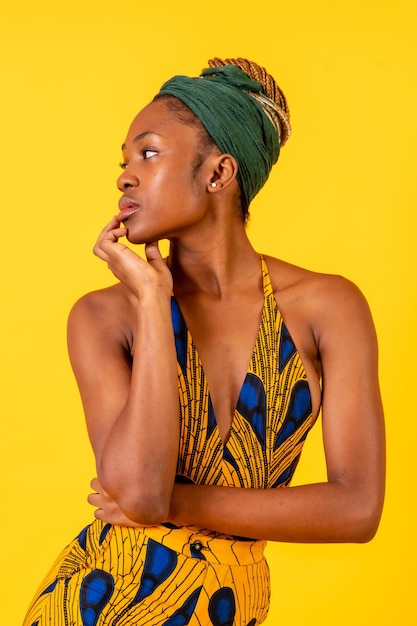 Jovem africana no estúdio em um retrato de fundo amarelo em um traje tradicional olhando