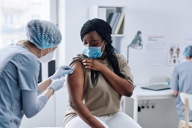 Jovem africana recebendo vacinação de braço com enfermeira durante sua visita ao hospital