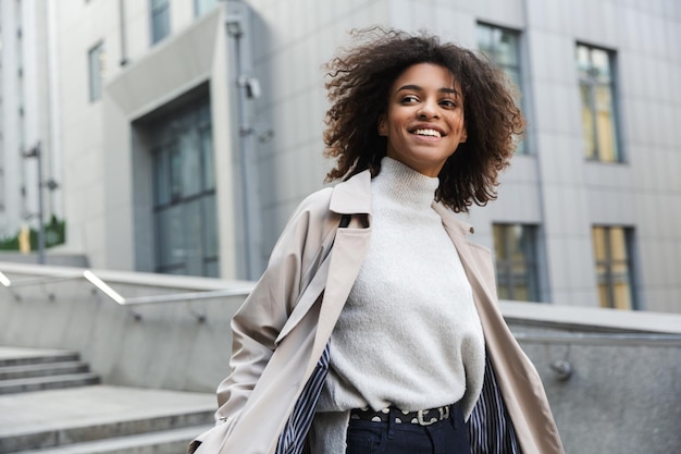 Jovem africana sorridente com um casaco de outono e caminhando ao ar livre