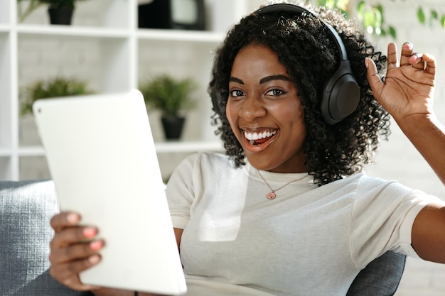 Jovem africana usando tablet digital e sorrindo enquanto descansava em casa