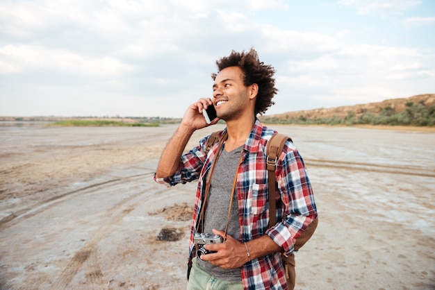 Jovem africano alegre com uma foto vintage em pé e falando no celular