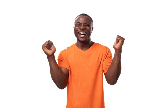 Jovem africano bonito e modesto, com corte de cabelo curto, vestindo camiseta laranja, esperando boa sorte