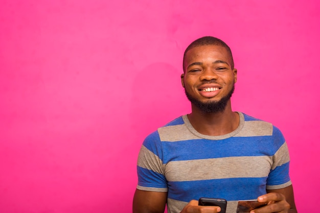 Jovem africano bonito isolado sobre um fundo rosa segurando seu cartão de crédito e telefone inteligente