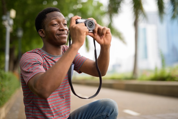 Jovem africano bonito tirando fotos com a câmera no parque