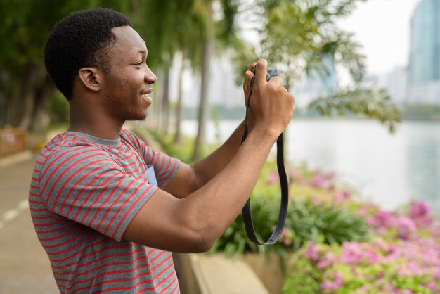 Jovem africano bonito tirando fotos com a câmera no parque