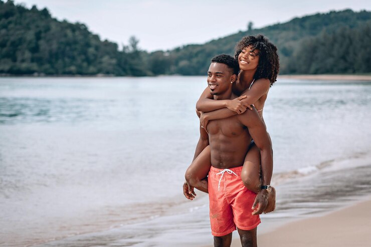 Jovem africano carregando sua namorada sorridente nas costas enquanto desfruta de um final de tarde juntos na praia. Phuket. Tailândia.