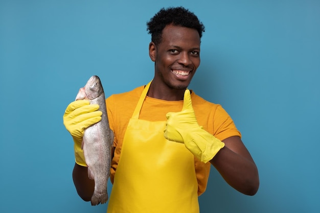 Foto jovem africano de avental amarelo com peixe salmão inteiro