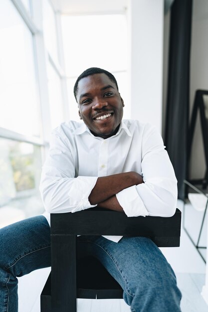 Foto jovem africano de camisa branca e óculos posando perto de uma grande janela