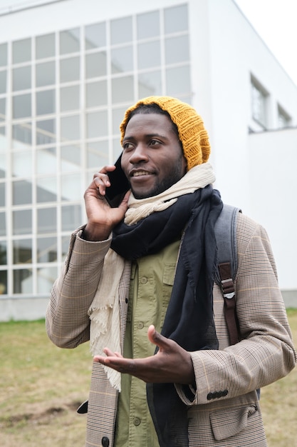 Jovem africano de chapéu falando no celular em pé na cidade