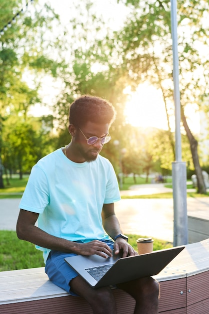 Jovem africano digitando em um laptop e trabalhando online enquanto está sentado no parque