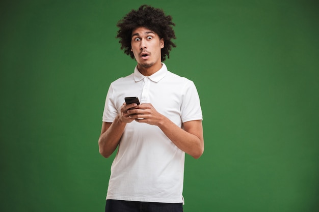 Jovem africano encaracolado chocado conversando pelo telefone celular.