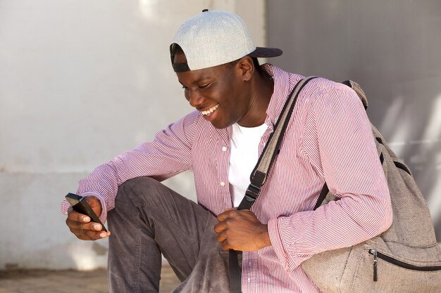 Jovem, africano, estudante masculino, com, boné, sorrindo, e, olhar, cellphone