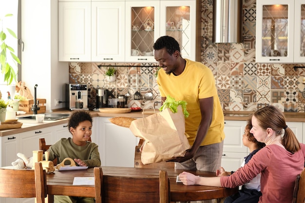 Jovem africano feliz segurando um grande saco de papel com produtos frescos do supermercado