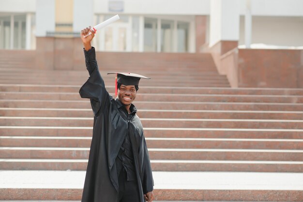 Jovem africano graduado do sexo masculino em frente ao prédio da universidade