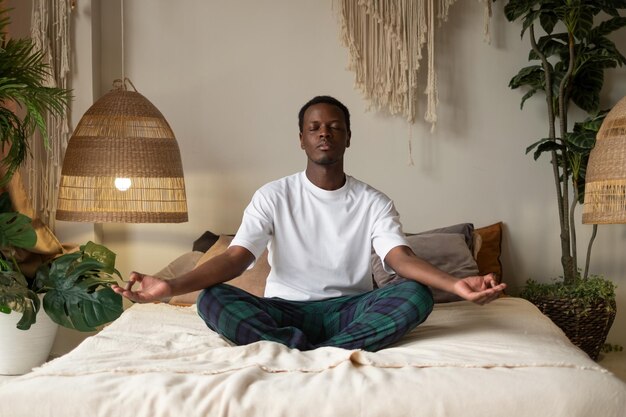 Jovem africano meditando sentado em seu quarto de manhã sozinho