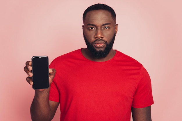 Jovem africano mostra visor de celular isolado em fundo rosa