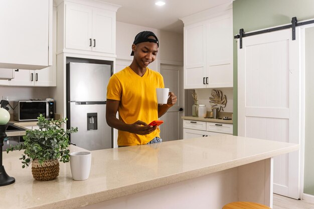 Jovem africano na cozinha com uma xícara de café e usando um telefone