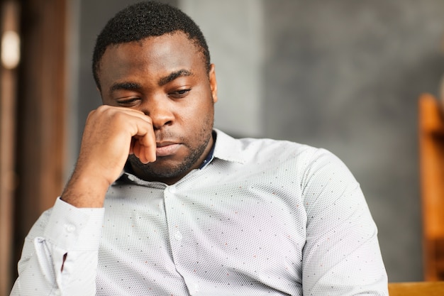 Jovem africano sentado com uma expressão triste ou pensando em algo