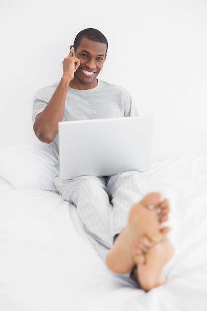 Jovem africano usando celular e laptop na cama