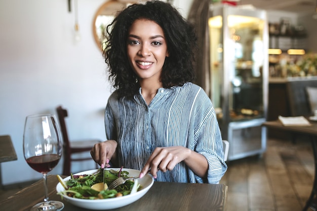 Jovem afro-americana com cabelo escuro e encaracolado sentada em um restaurante