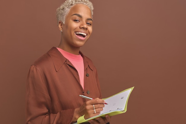 Jovem afro-americana com caderno e caneta nas mãos fica no estúdio