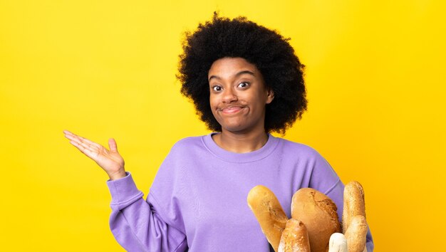 Jovem afro-americana comprando algo pão isolado em amarelo fazendo gesto de dúvida