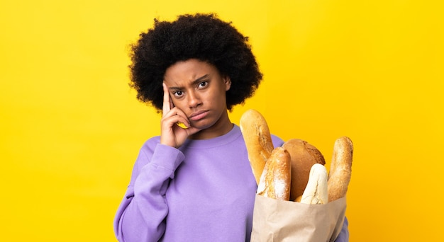 Jovem afro-americana comprando algo pão isolado em um fundo amarelo, pensando em uma ideia