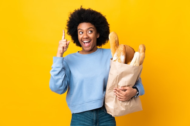 Jovem afro-americana comprando um pão isolado no amarelo com a intenção de perceber a solução enquanto levanta um dedo