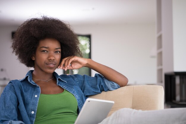 Jovem afro-americana em casa relaxando em sua luxuosa sala de estar lendo um tablet digital PC navegar na internet e trabalhar