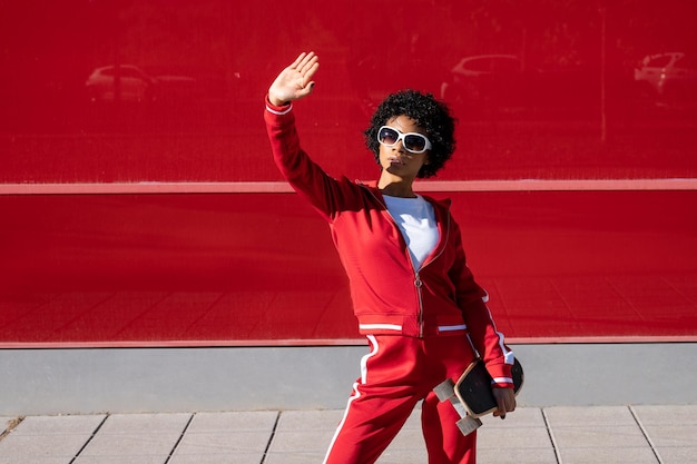 Jovem afro-americana em roupas esportivas e um skate em um fundo de cor vermelha