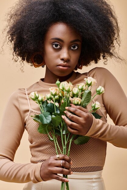 jovem afro-americana encaracolada segurando pequenas rosas em fundo bege cor de pêssego fuzz