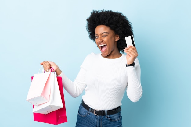 Jovem afro-americana isolada em azul segurando sacolas de compras e um cartão de crédito