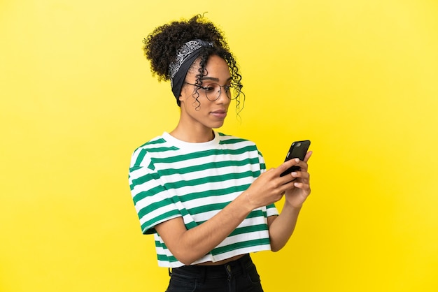 Jovem afro-americana isolada em fundo amarelo enviando uma mensagem ou e-mail com o celular