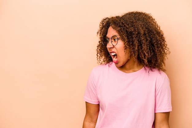 Jovem afro-americana isolada em fundo bege gritando conceito de raiva muito irritado frustrado